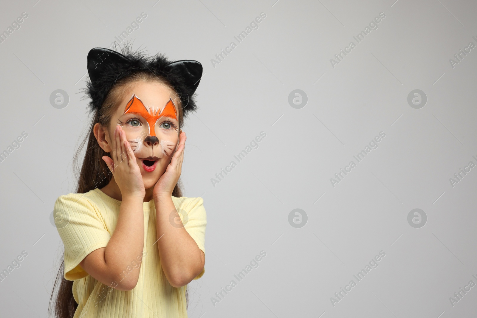 Photo of Cute girl with painted face and ears as cat on grey background, space for text