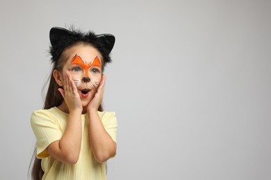 Photo of Cute girl with painted face and ears as cat on grey background, space for text