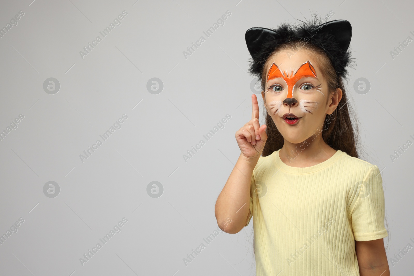 Photo of Cute girl with painted face and ears as cat on grey background, space for text