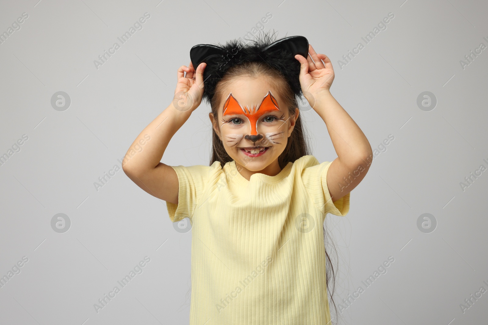 Photo of Cute girl with painted face and ears as cat on grey background