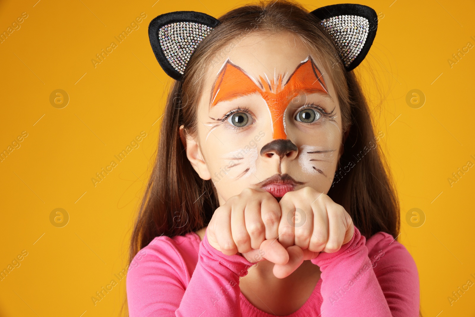 Photo of Cute girl with painted face and ears as cat on orange background