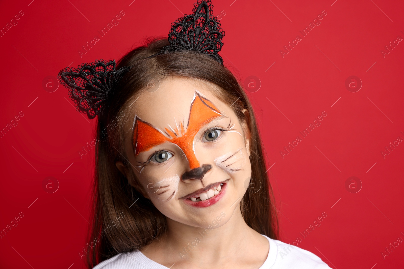 Photo of Cute girl with painted face and ears as cat on red background, closeup