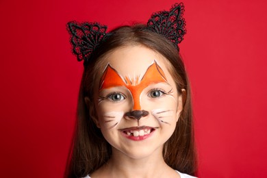 Photo of Cute girl with painted face and ears as cat on red background, closeup