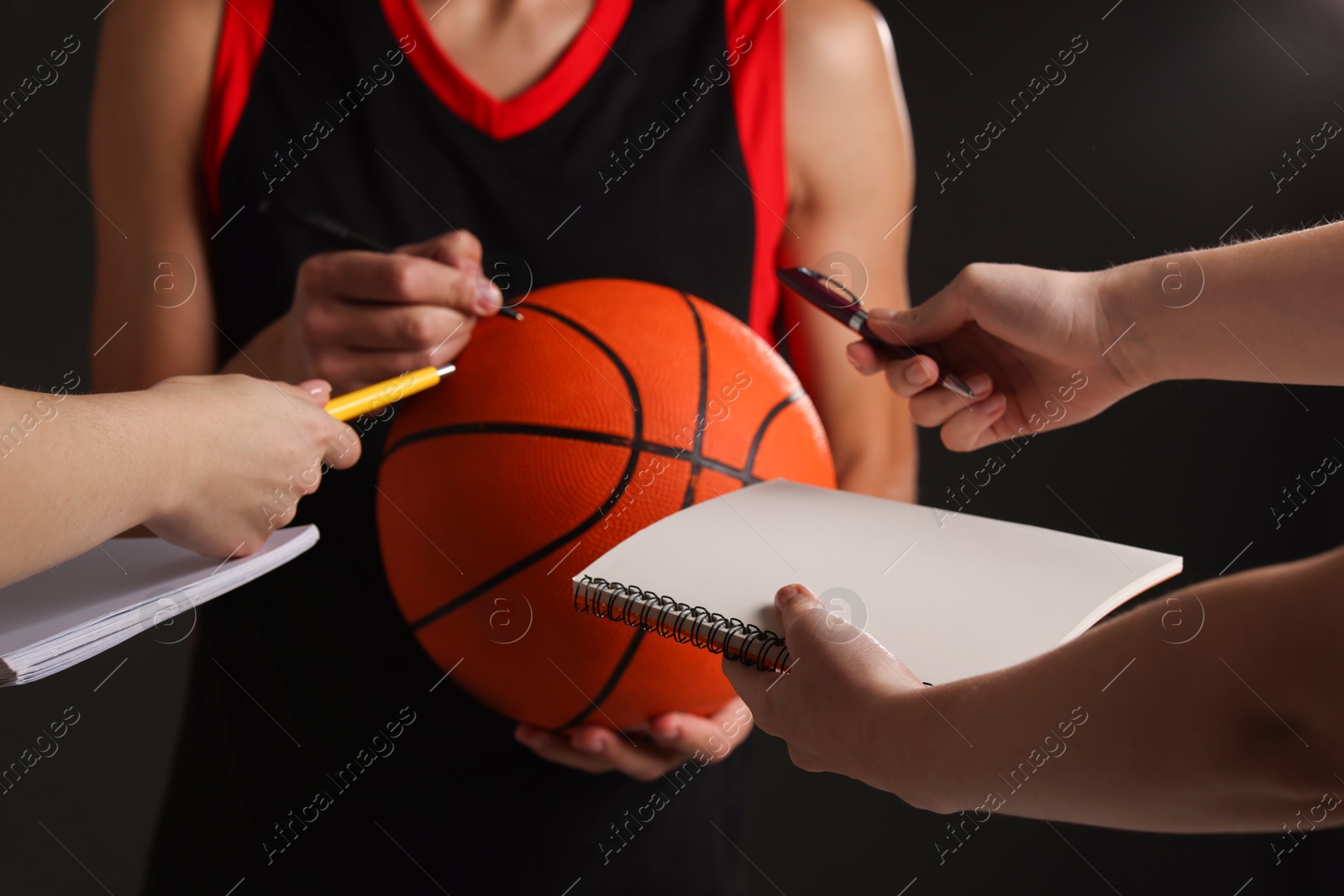 Photo of Sportsman signing autograph on basketball ball against black background, closeup