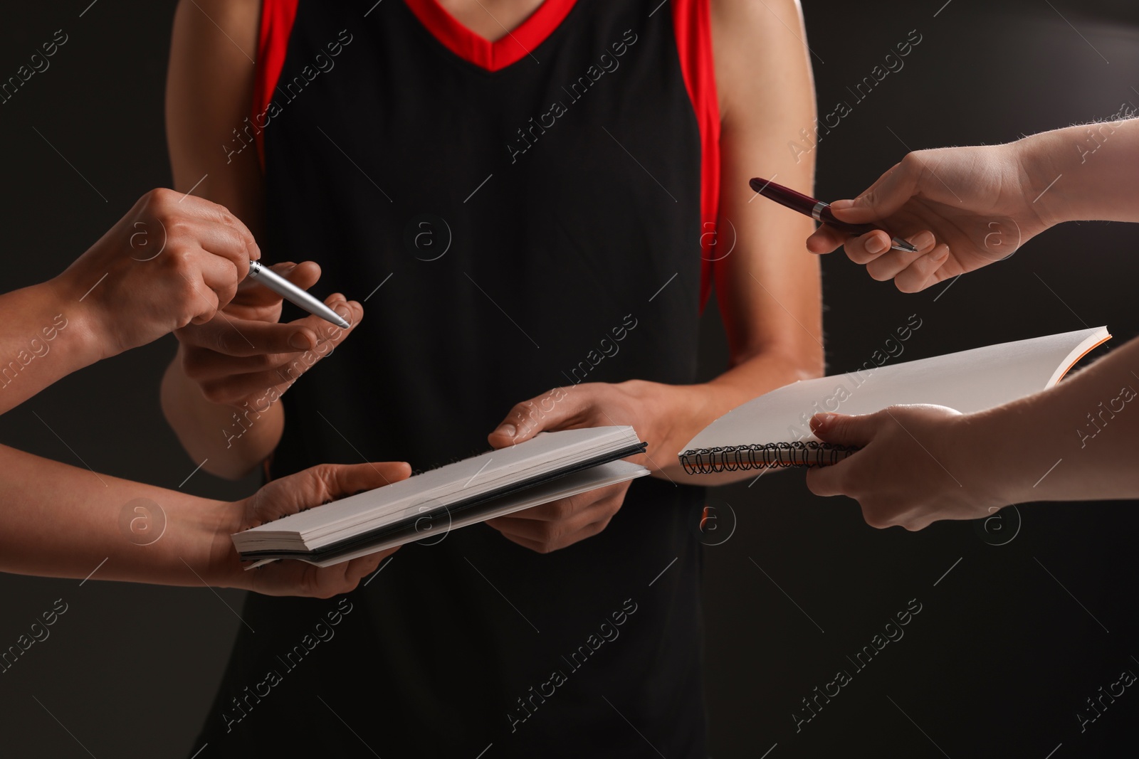 Photo of Sportsman signing autograph in notebooks on black background, closeup