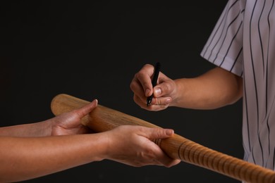 Photo of Baseball player signing autograph on bat against black background, closeup