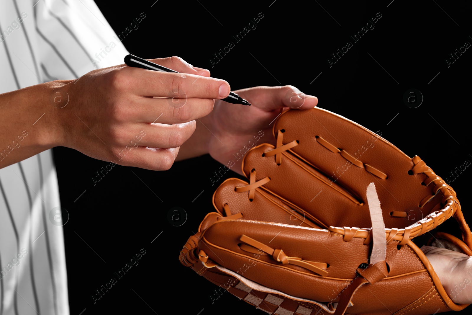 Photo of Baseball player signing autograph on leather glove against black background, closeup