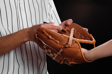 Photo of Baseball player signing autograph on leather glove against black background, closeup