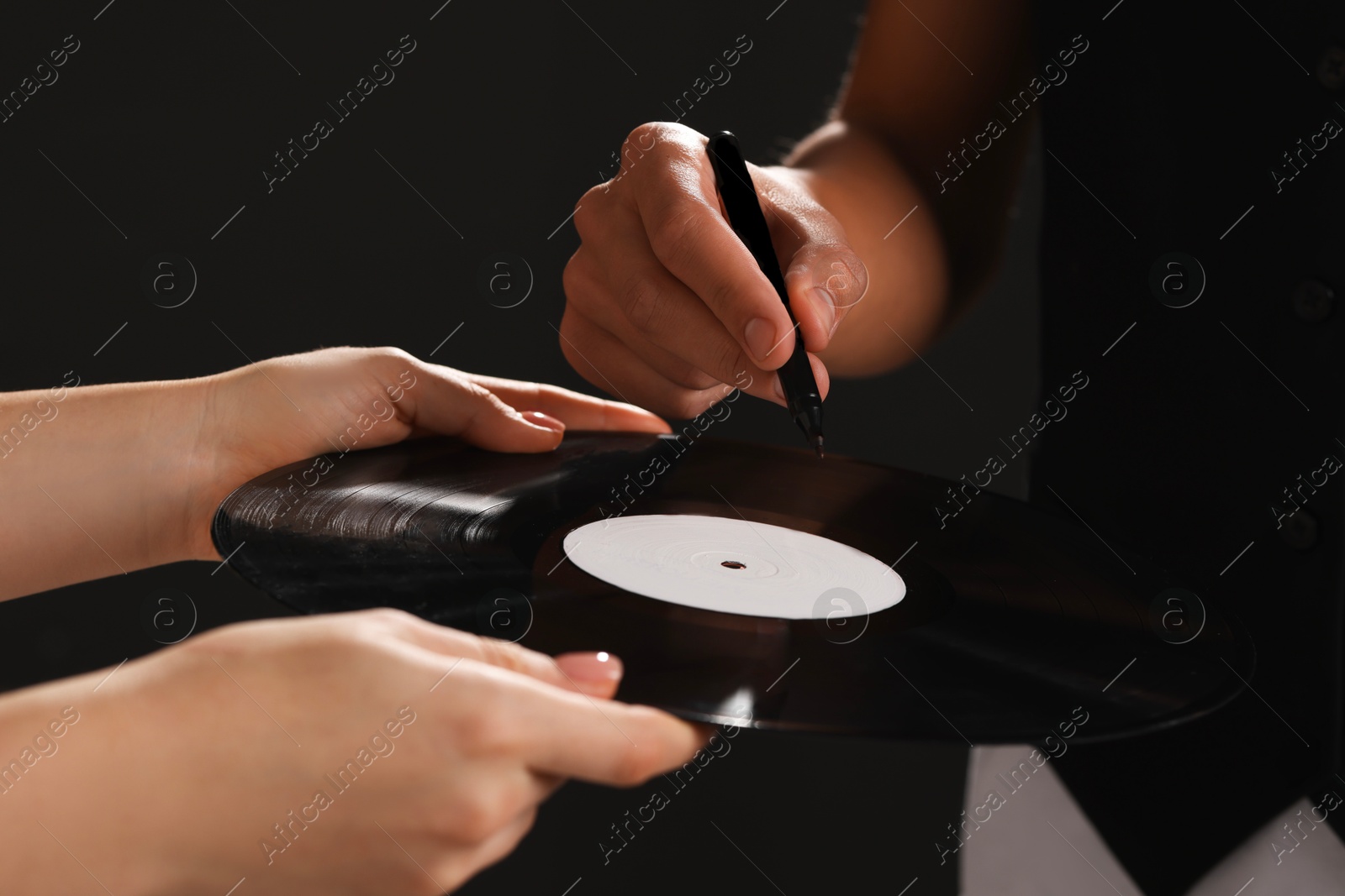 Photo of Singer signing autograph on vinyl record against dark background, closeup