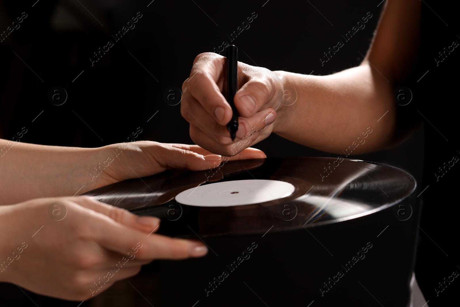 Photo of Singer signing autograph on vinyl record against dark background, closeup