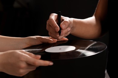 Photo of Singer signing autograph on vinyl record against dark background, closeup