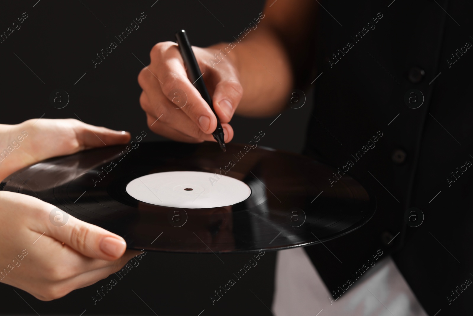 Photo of Singer signing autograph on vinyl record against black background, closeup