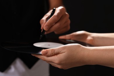 Photo of Singer signing autograph on vinyl record against black background, closeup