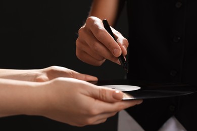 Photo of Singer signing autograph on vinyl record against black background, closeup