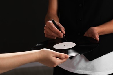 Photo of Singer signing autograph on vinyl record against black background, closeup