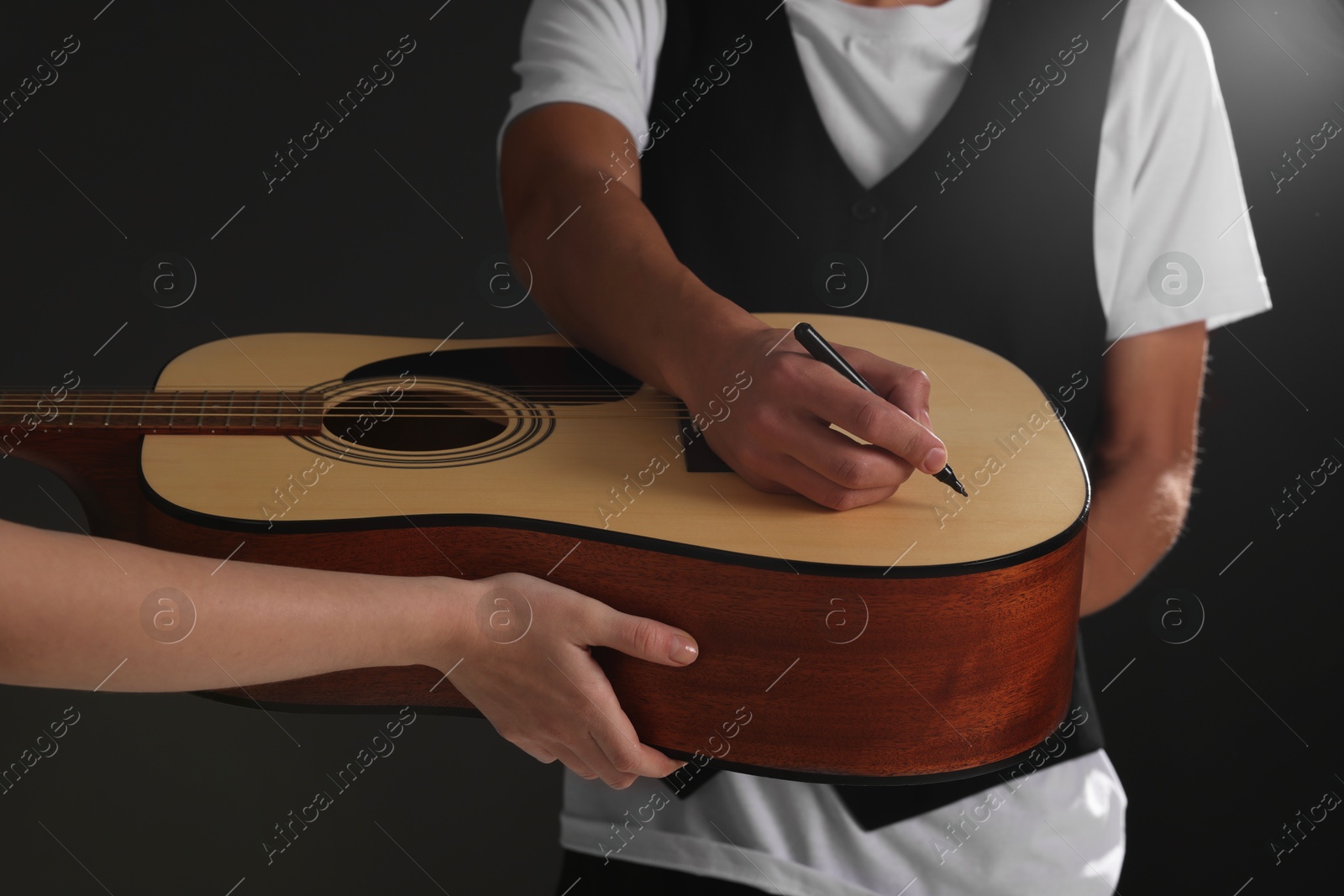 Photo of Musician signing autograph on guitar against dark background, closeup