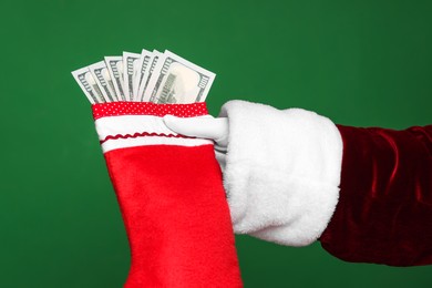 Photo of Santa Claus holding stocking with dollar banknotes on green background, closeup