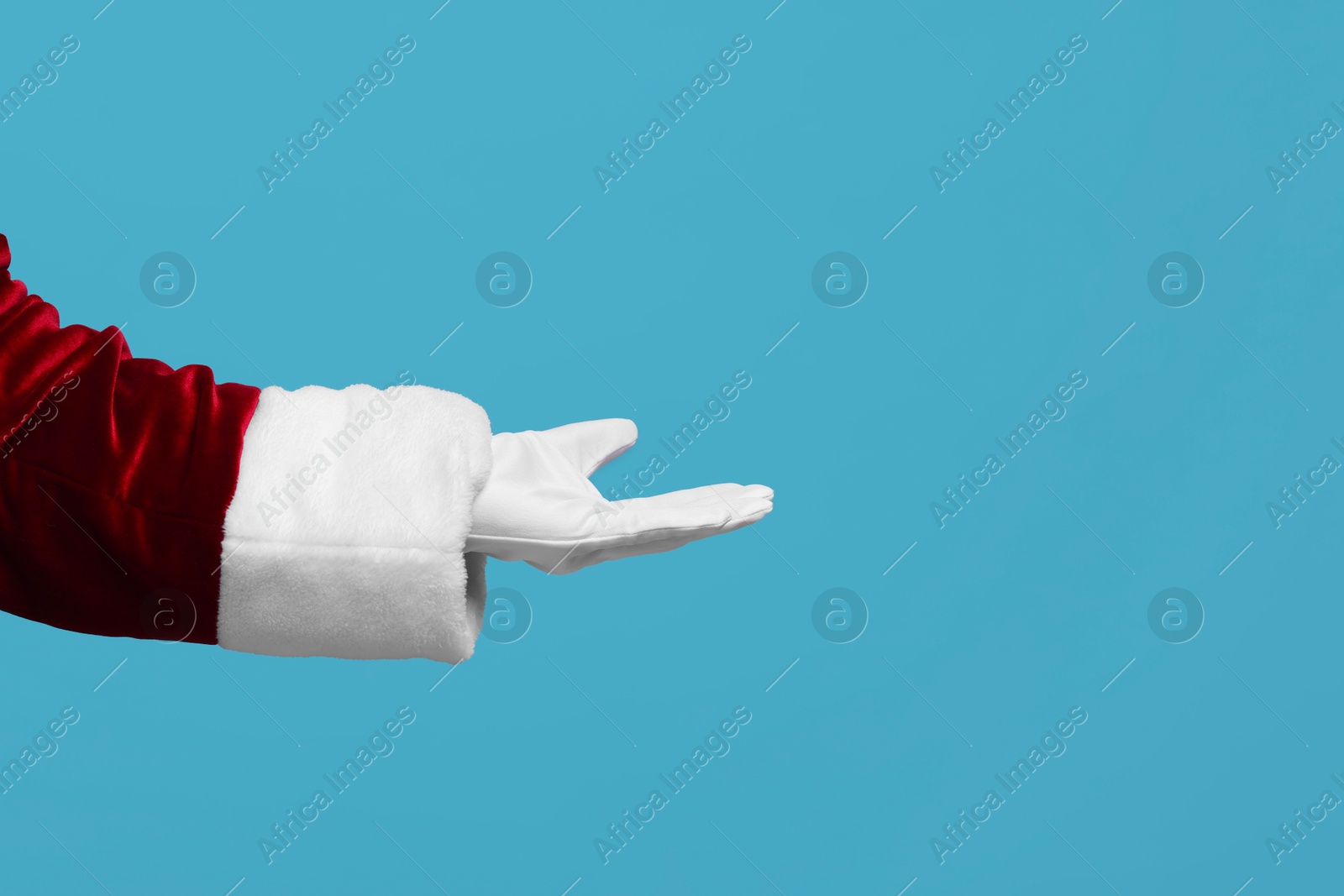 Photo of Santa Claus holding something on light blue background, closeup. Space for text