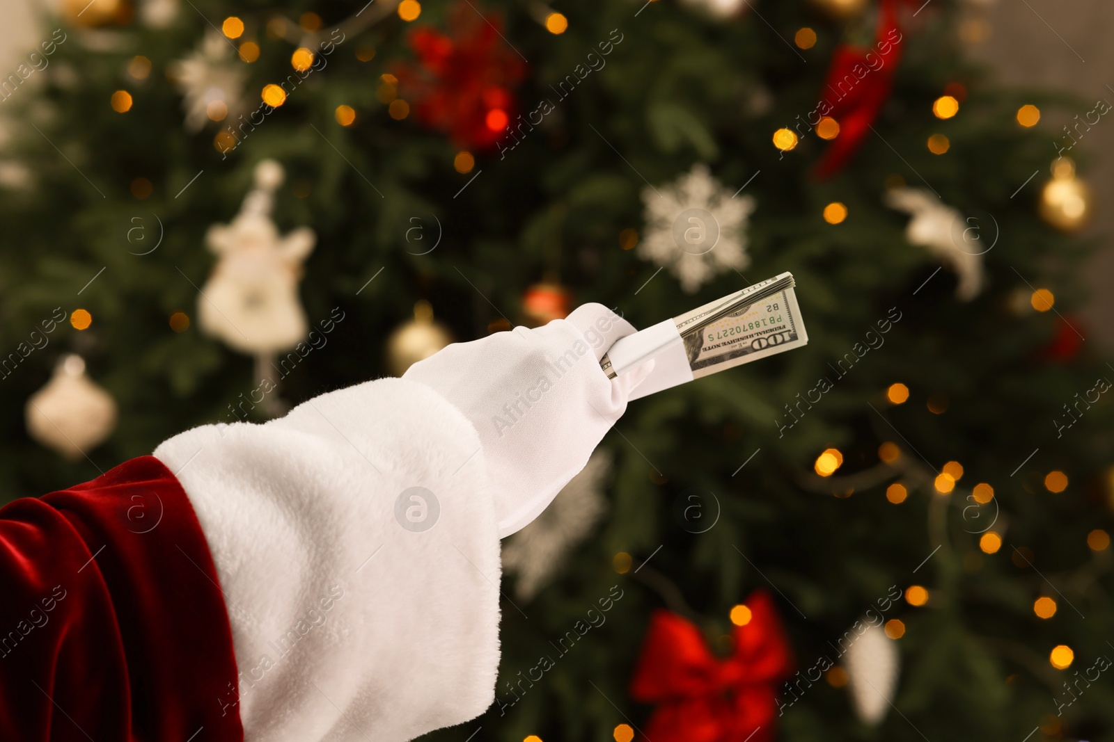 Photo of Santa Claus with dollar banknotes near Christmas tree indoors, closeup