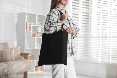 Photo of Woman with blank black shopper bag indoors, closeup. Mockup for design