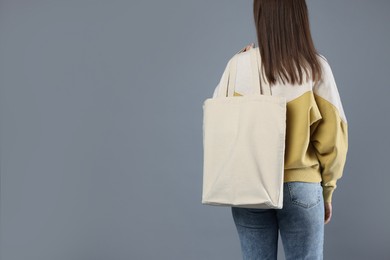 Woman with blank shopper bag on grey background, back view. Mockup for design