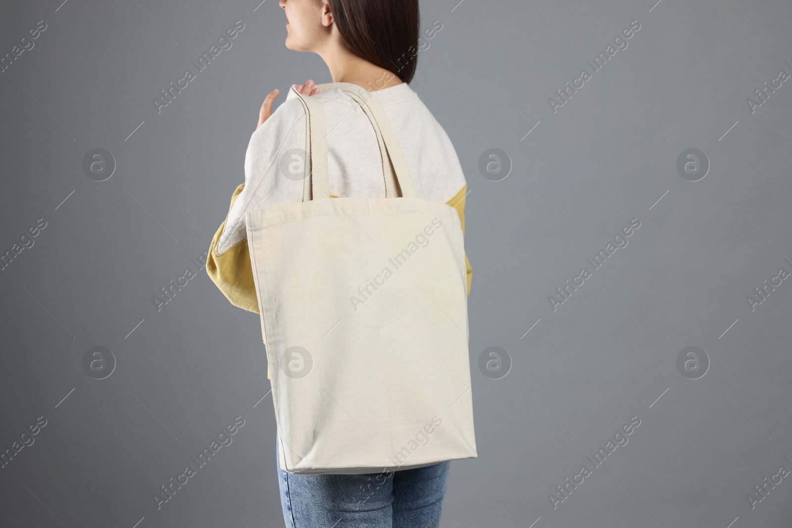 Photo of Woman with blank shopper bag on grey background, back view. Mockup for design