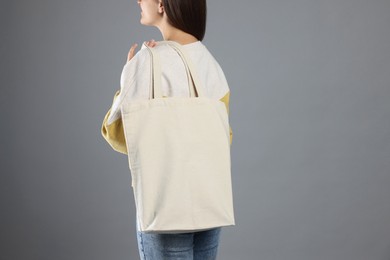 Photo of Woman with blank shopper bag on grey background, back view. Mockup for design