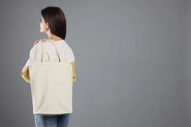 Photo of Woman with blank shopper bag on grey background, back view. Mockup for design