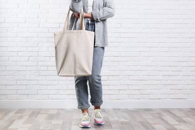 Photo of Woman with blank shopper bag near white brick wall, closeup. Mockup for design