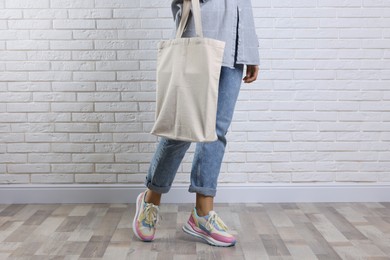 Photo of Woman with blank shopper bag near white brick wall, closeup. Mockup for design