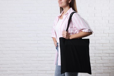 Woman with blank black shopper bag near white brick wall, closeup. Mockup for design