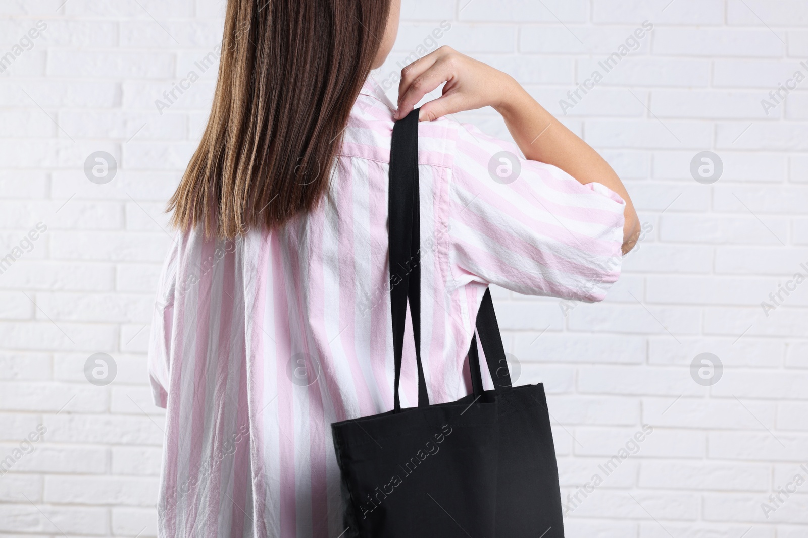 Photo of Woman with blank black shopper bag near white brick wall, back view. Mockup for design