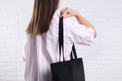 Woman with blank black shopper bag near white brick wall, back view. Mockup for design