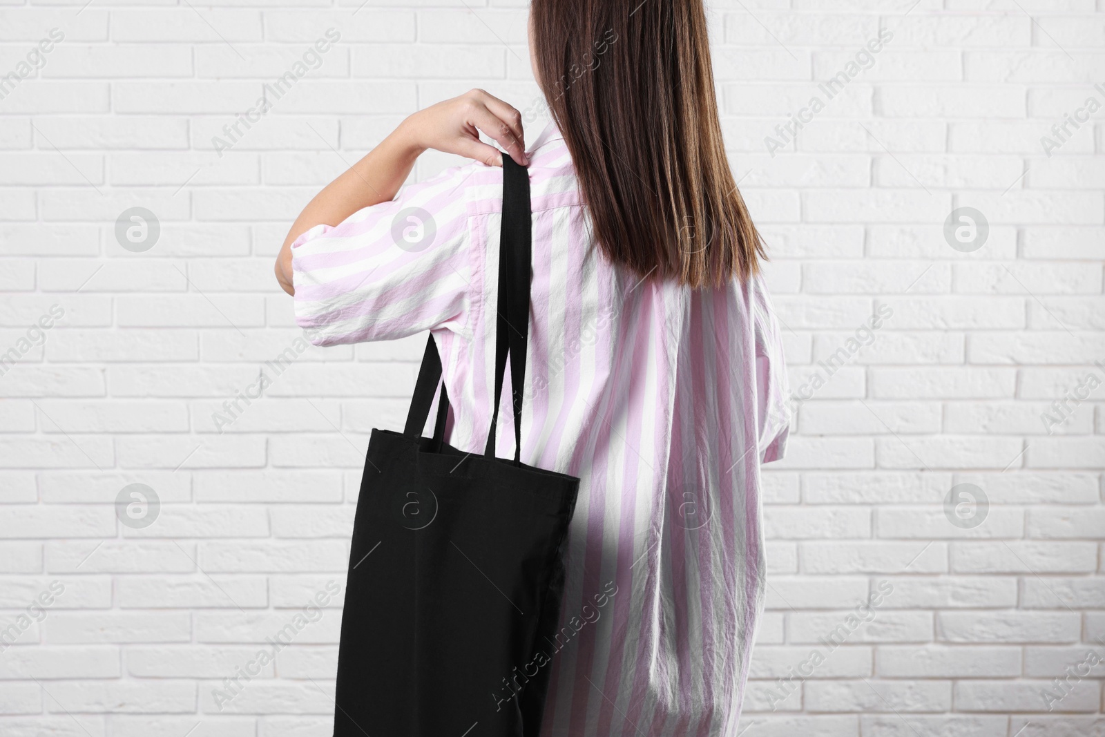 Photo of Woman with blank black shopper bag near white brick wall, back view. Mockup for design