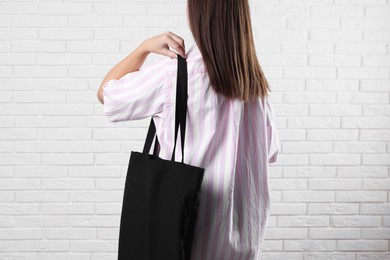 Photo of Woman with blank black shopper bag near white brick wall, back view. Mockup for design