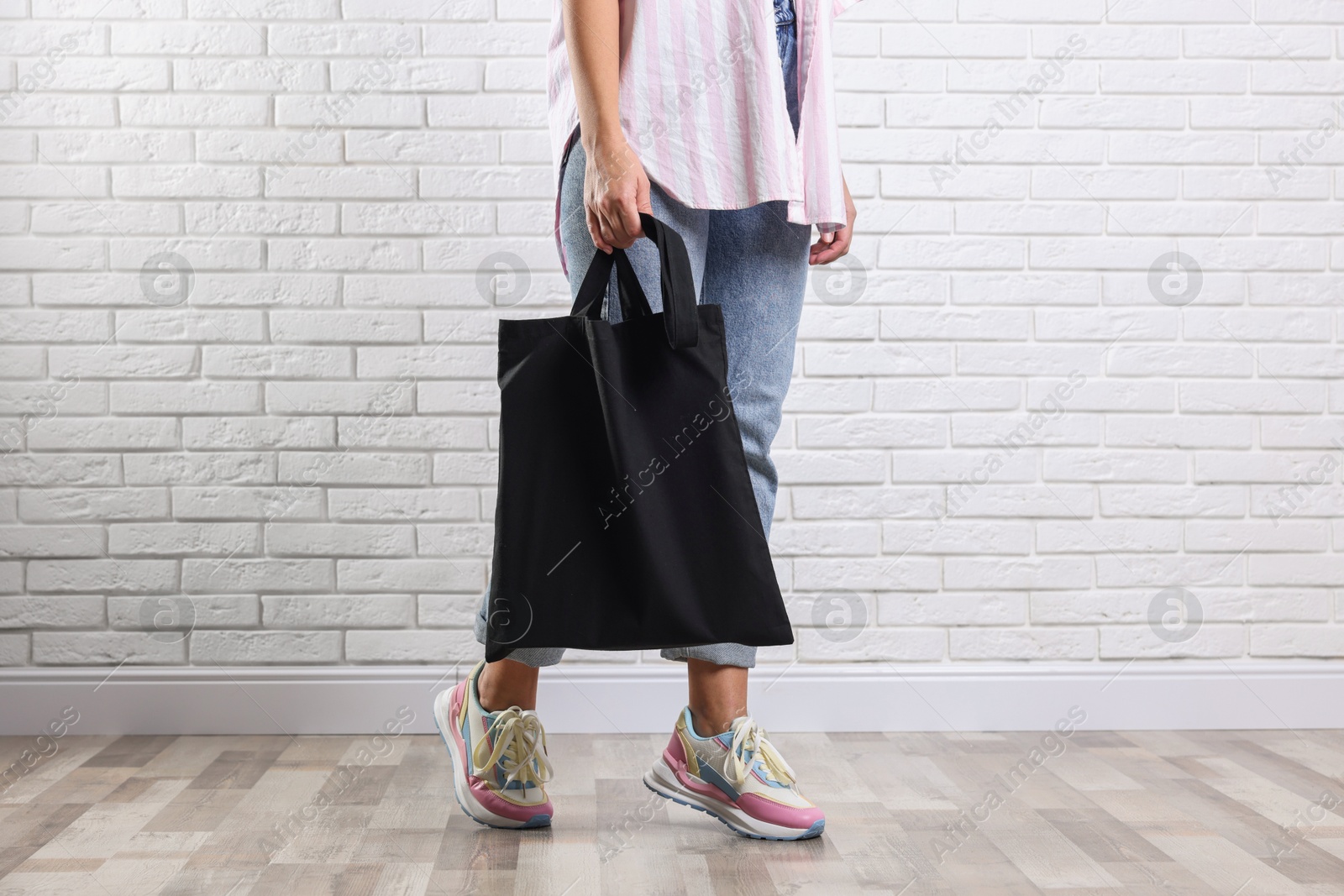 Photo of Woman with blank black shopper bag near white brick wall, closeup. Mockup for design