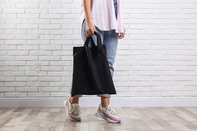 Photo of Woman with blank black shopper bag near white brick wall, closeup. Mockup for design