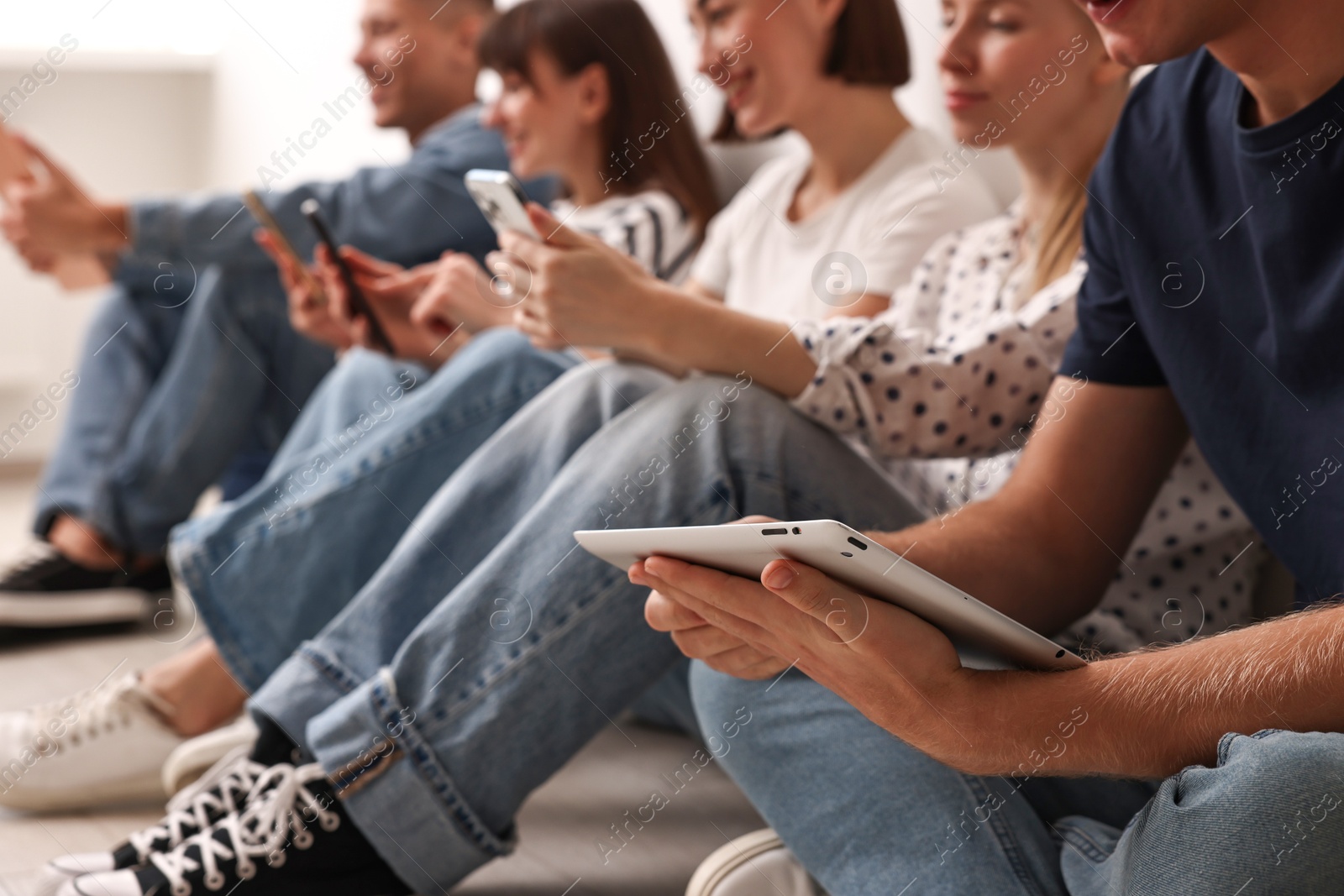 Photo of Group of people using different gadgets on floor indoors, closeup. Modern technology