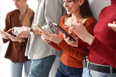 Photo of Group of people using different gadgets near light wall indoors, closeup. Modern technology