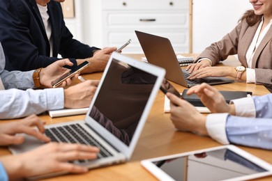 Photo of Group of people using different gadgets at wooden table in office, closeup. Modern technology