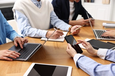 Photo of Group of people using different gadgets at wooden table in office, closeup. Modern technology