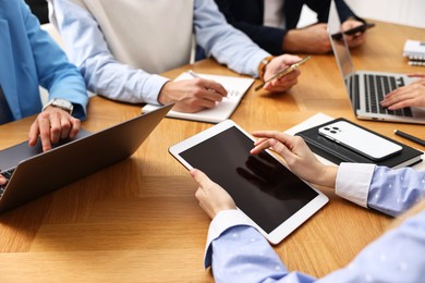 Photo of Group of people using different gadgets at wooden table in office, closeup. Modern technology