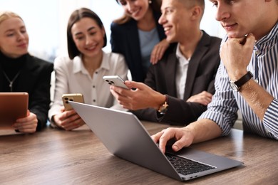 Group of people using different gadgets at wooden table in office, selective focus. Modern technology