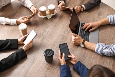 Group of people using different gadgets at wooden table in office, closeup. Modern technology