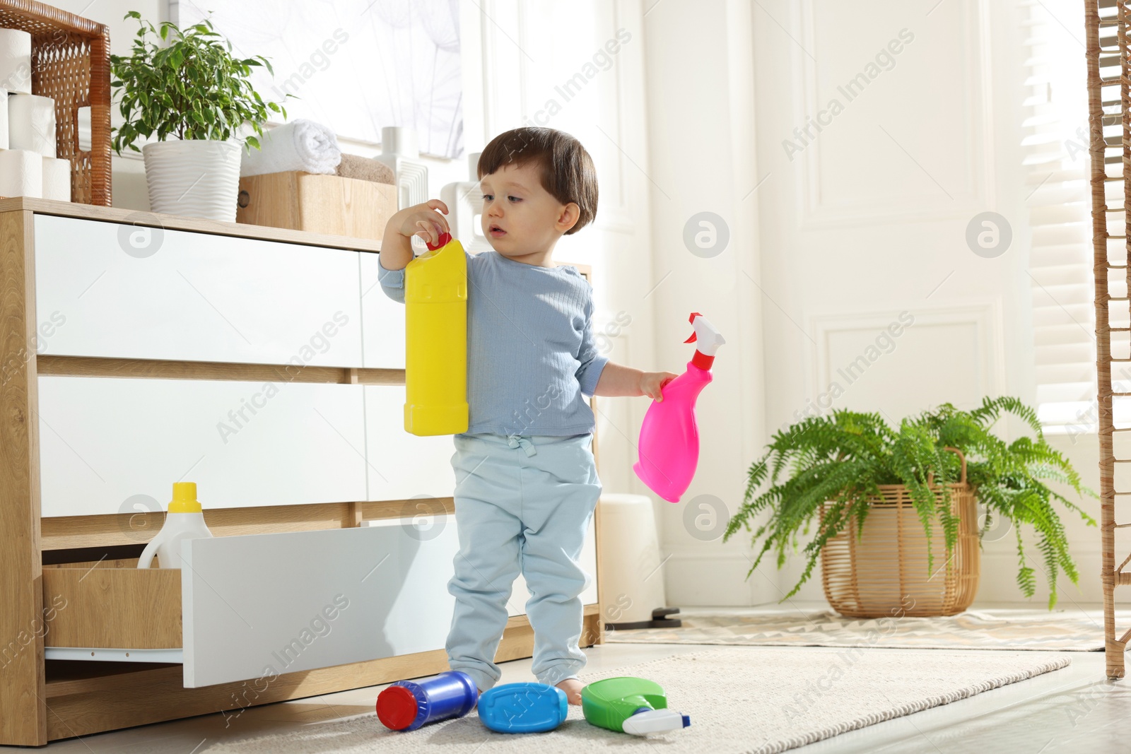 Photo of Little boy playing with bottles of detergents near cabinet at home. Child in danger