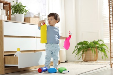 Photo of Little boy playing with bottles of detergents near cabinet at home. Child in danger