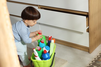 Photo of Little boy playing with bottles of detergents near cabinet at home. Child in danger