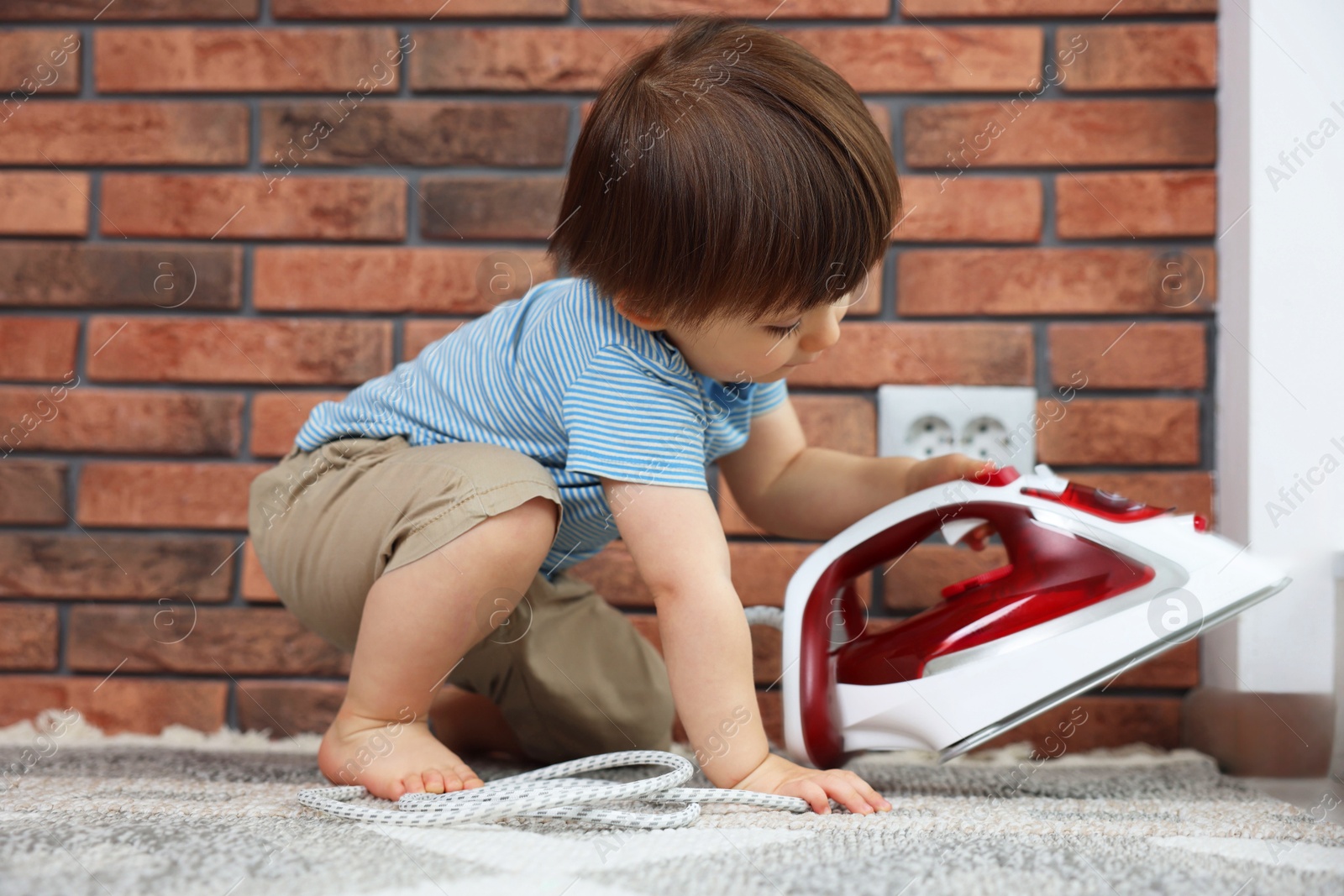 Photo of Little boy playing with iron near electrical socket at home. Child in danger