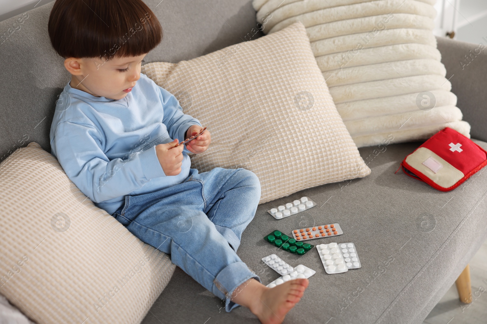 Photo of Little boy playing with pills on sofa at home. Child in danger