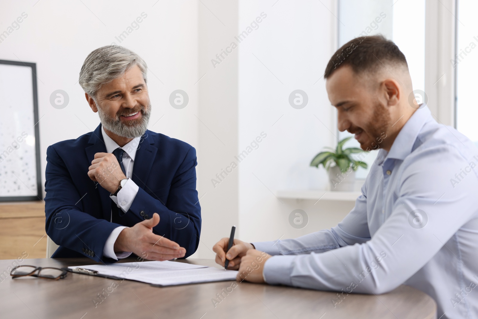 Photo of Client signing notarial paperwork during meeting with lawyer at wooden desk indoors, selective focus